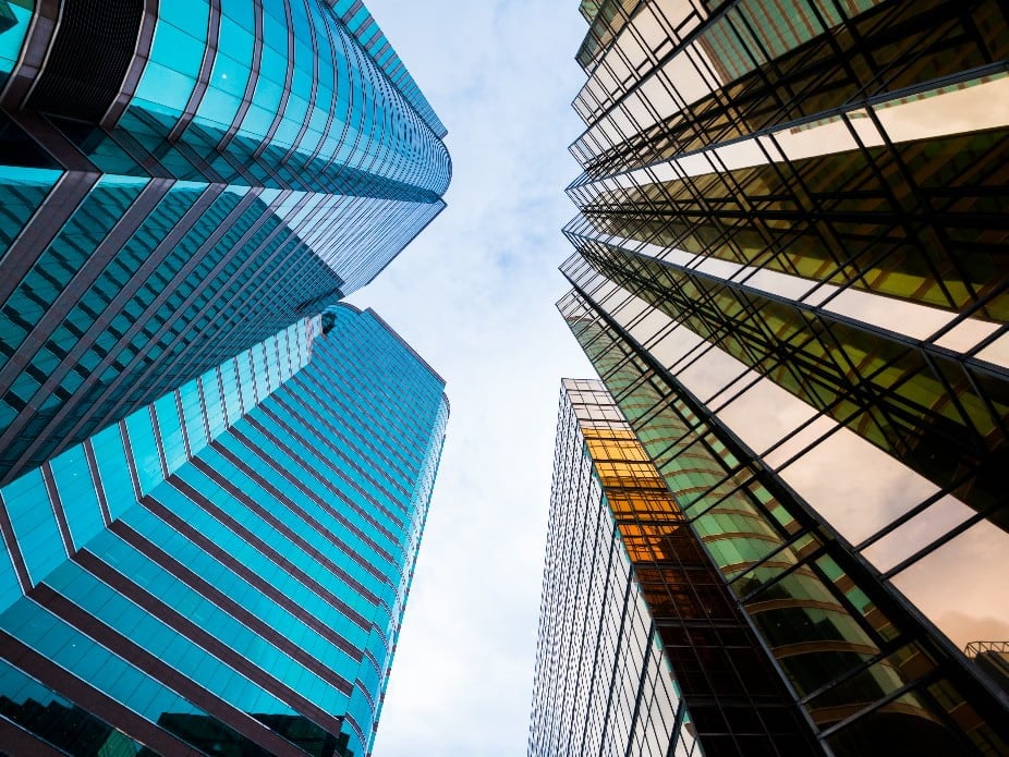looking up at the sky with cool blue colored building on the left and warm brown building on right